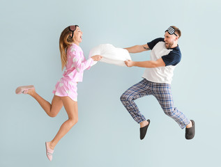 Young couple fighting for pillow on color background