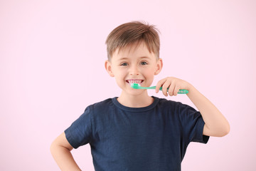 Portrait of little boy brushing teeth on color background