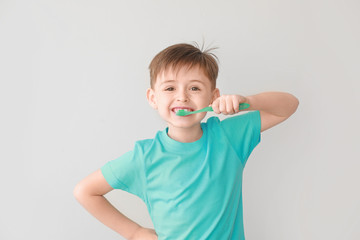 Portrait of little boy brushing teeth on light background