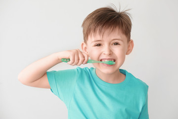 Portrait of little boy brushing teeth on light background