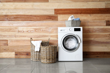 Modern washing machine with laundry near wooden wall