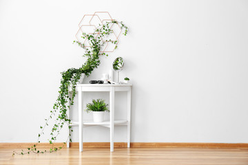 Dressing table with green houseplants near white wall