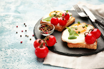 Slate plate with tasty sandwiches on color background