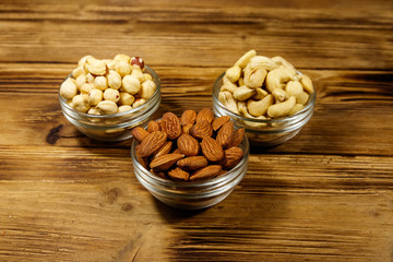 Assortment of nuts on wooden table. Almond, hazelnut and cashew in glass bowls. Healthy eating concept