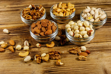Assortment of nuts on wooden table. Almond, hazelnut, pistachio, walnut and cashew in glass bowls. Healthy eating concept