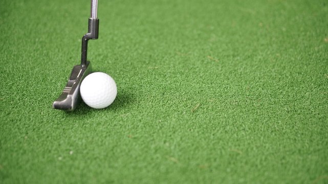 Image of golf putter and golf ball on green grass
