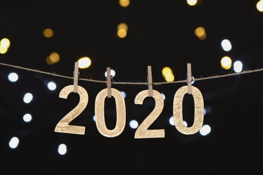 Año nuevo de 2020 en letras de madera dorada colgando de una cuerda con luces desenfocadas sobre fondo negro
