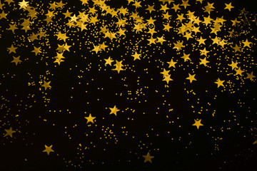 gold star confetti and glitter on a black background - Christmas / New Year party festive backdrop for your projects