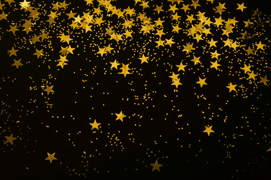 gold star confetti and glitter on a black background - Christmas / New Year party festive backdrop for your projects