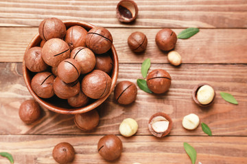 Bowl with tasty macadamia nuts on wooden background