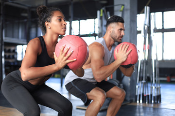 Beautiful young sports couple is working out with medicine ball in gym.