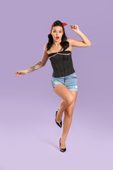 Naklejka premium Portrait of beautiful tattooed pin-up woman on color background