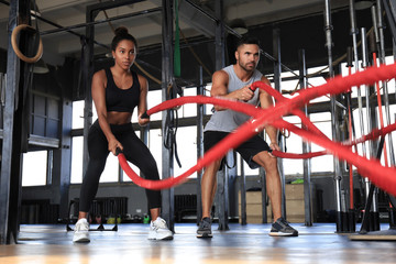 Athletic young couple with battle rope doing exercise in functional training fitness gym.