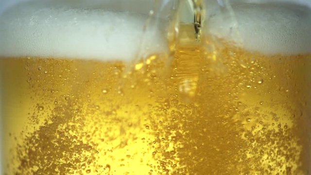 Close up shot of pouring beer with bubbles and foam in glass, slow motion