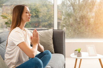 Beautiful young woman meditating at home