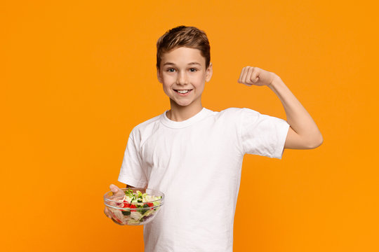 Teen boy with fresh vegetable salad demonstrating his biceps