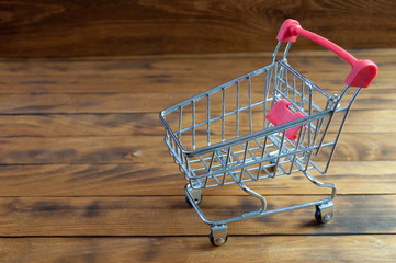 Empty shopping cart on wooden background. Small trolley. Shopping and money spending concept.