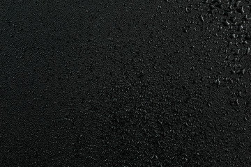 A dark abstract background of water drops on flat black rubber surface