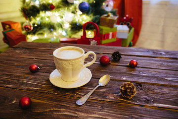Mug with hot chocolate on a wooden table with Christmas decorations on a background of the Christmas tree
