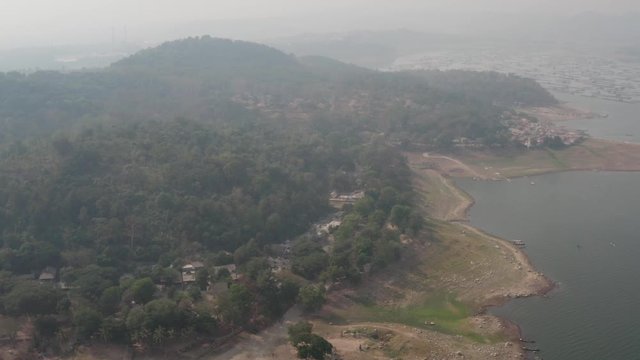 Aerial of dense forest island shore on hazy day, West Java, dolly in