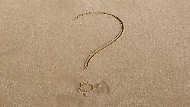 Handwritten inscription of question mark on a sandy sea beach is wiped by the sea wave with foam on a summer sunny day. 