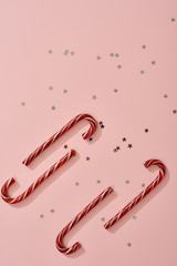 Christmas background with Xmas candy canes and star confetti. Top view, flat lay. Christmas candy cane on pink background. Copy space for text.