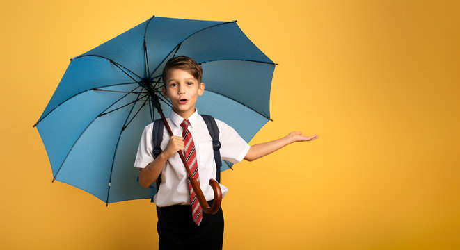 Child student with blue umbrella on yellow background. Amazed expression