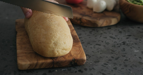 man cuts ciabatta bread on olive board