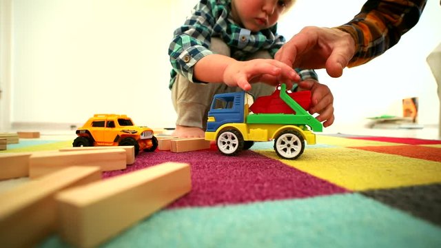 Closeup of little boy hands playing with car and wooden constructor building house at home with sunny modern kids room on background. Happy family. Children mind development. Parenting lifestyle.