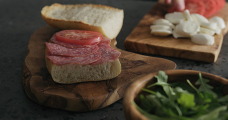 man put tomato on ciabatta slice on olive board