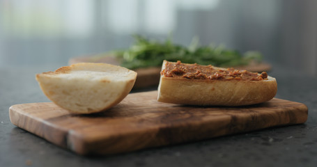 man spread red pesto on ciabatta slice on olive board