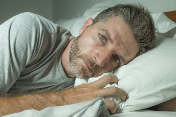 dramatic portrait of stressed and frustrated man in bed awake at night suffering insomnia sleeping...