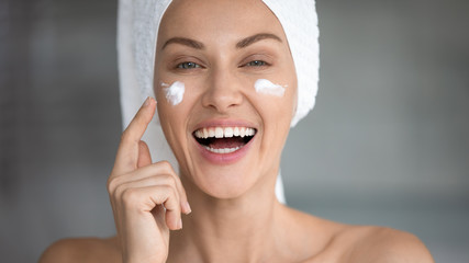 Cheerful attractive young woman apply facial creme looking at camera