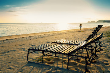 Two wooden deck chairs on the sandy seashore at sunset, image with retro toning