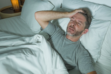 Fototapeta premium dramatic portrait of stressed and frustrated man in bed awake at night suffering insomnia sleeping disorder tired and desperate unable sleep feeling exhausted