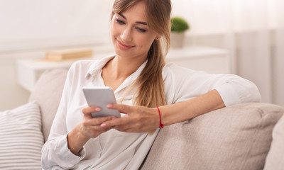 Female Entrepreneur Using Smartphone Reading News Sitting On Sofa Indoor