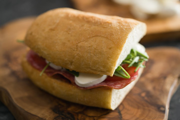 closeup ciabatta sandwich with salami and mozzarella cheese on olive board