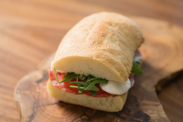 ciabatta sandwich with salami and mozzarella cheese on walnut table