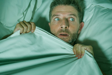  stressed and scared man alone in bed awake at night in fear after having a nightmare feeling...