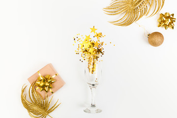 Glass of champagne with glitter and holiday decorations and gift box on a white background, top view. New Year or Christmas