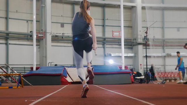 Pole vaulting indoors - a young woman with ponytail running up and jumping over the bar