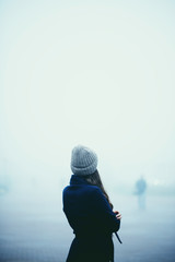 Girl in a warm blue coat and hat in a foggy city