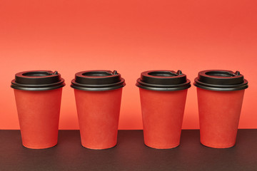 Red disposable paper cup for takeaway drinks. Mockup red paper cup on red and black background.