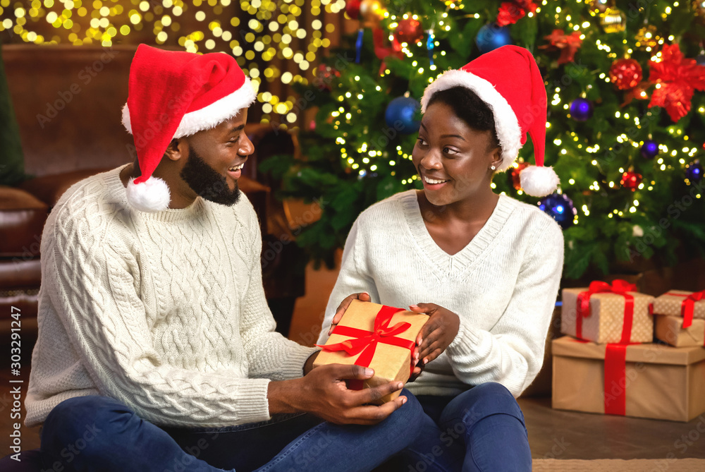 Wall mural Happy afro woman receiving Christmas present from her loving husband