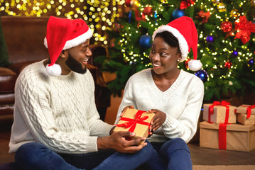 Obraz na płótnie Canvas Happy afro woman receiving Christmas present from her loving husband