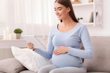 Pregnant Girl Using Digital Tablet Sitting On Sofa At Home