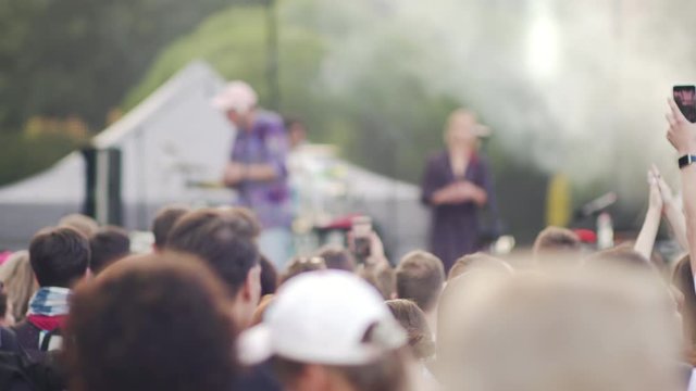 Young man and woman dancing, recording video using smartphone at rock concert. American people fans enjoying live music, waving hand, taking photo in front of stage at summer musical festival. Concept