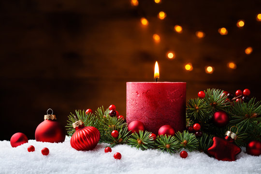 Advent candle, fir tree branches and holiday decorations in snow against light  garland background. Christmas card.