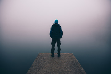 Man standing on a deck above a misty lake. Depression and suicide concept. - obrazy, fototapety, plakaty