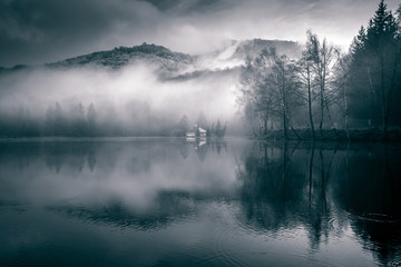 Foggy day at a lake with a little island with a church in the middle. Mogoasa, Romania.
